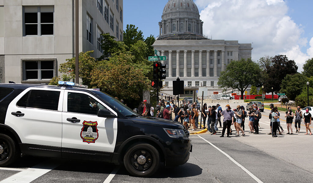 A Jefferson City police SUV passes by protesters crossing Capitol Avenue near the Missouri State Capitol